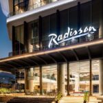 Radisson Hotel Group annonce l’expansion de sa marque Radisson Individuals, qui compte désormais plus de 100 hôtels en exploitation et en développement depuis son lancement en 2020. Cette marque flexible et innovante séduit les voyageurs en offrant des expériences uniques et des hôtels au caractère authentique à travers le monde. Une marque flexible pour hôtels indépendants Radisson Individuals permet aux hôtels indépendants et aux chaînes régionales de rejoindre le réseau mondial de Radisson Hotel Group, tout en conservant leur identité et leur personnalité unique. Les établissements bénéficient ainsi de la notoriété internationale, des programmes de formation et du service emblématique Yes I Can!. Nouveaux segments pour plus de diversité La marque s’étend désormais sur trois segments : Radisson Individuals Premier : hôtels haut de gamme supérieur, idéals pour les séjours d’affaires et de loisirs. Radisson Individuals Boutique : hôtels intimistes et élégants, offrant un charme local et authentique. Radisson Individuals Retreats : retraites et escapades immersives, pour ressourcer corps et esprit dans des destinations exceptionnelles. Exemples récents d’ouverture Parmi les nouvelles adresses : Le Relais de La Malmaison près de Paris – une expérience paisible et raffinée. HARBR Hotel Ludwigsburg, à Stuttgart – hôtel urbain contemporain. Crystals Beach Resort Belle Mare, Île Maurice – immersion sur la côte est. Namah Nainital, Inde – quatrième hôtel Radisson Retreats dans l’État d’Uttarakhand. Témoignage du groupe Elie Younes, Vice-président exécutif et Directeur mondial du développement de Radisson Hotel Group, déclare : « Radisson Individuals offre aux hôtels indépendants une visibilité mondiale et des opportunités uniques tout en conservant leur authenticité. L’expansion avec trois segments renforce notre offre et la différenciation des établissements. » Une opportunité pour les propriétaires Rejoindre Radisson Individuals permet aux propriétaires d’hôtels de : Accéder à la plateforme globale de distribution de Radisson Hotel Group. Offrir un service de qualité internationale aux voyageurs. Maintenir le caractère unique de chaque établissement. Avec Radisson Individuals, chaque hôtel conserve son identité tout en profitant de la force du réseau mondial, pour séduire une clientèle variée et exigeante.
